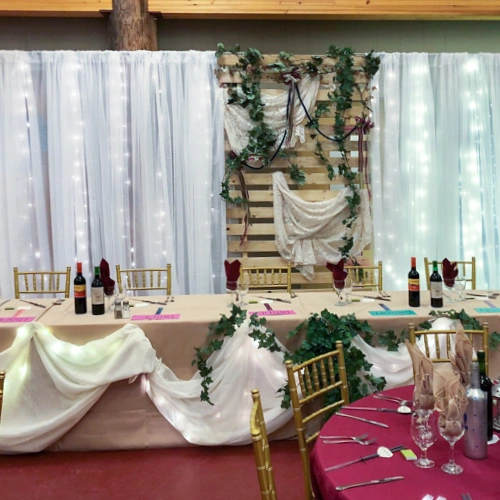 head table with chiavari chairs, organza backdrop with lights, and wood slat panel