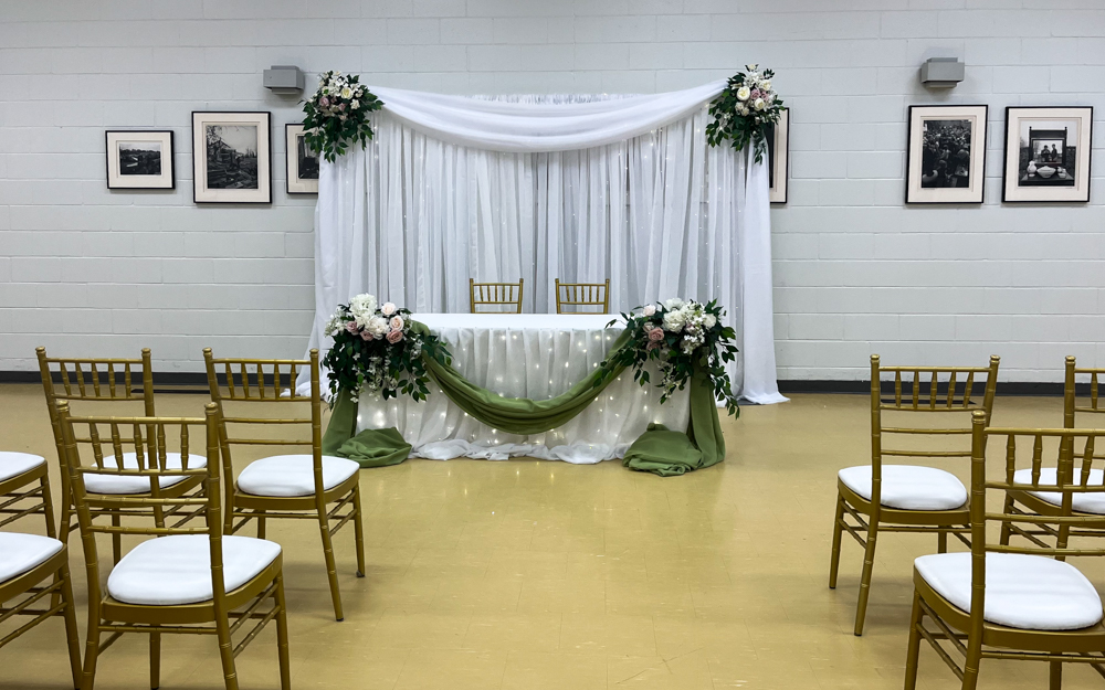 Weddings small head table with organza draping, mini lights, green accent fabric and flower bouquets. Organza backdrop with mini lights, chiavari chairs